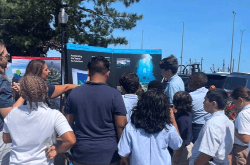 A group of students and adults looking at educational displays outdoors.