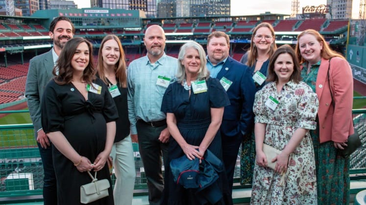 Group of people smiling at a baseball stadium with cityscape in the background