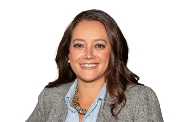 Person in a gray blazer and blue shirt, smiling against a white background.