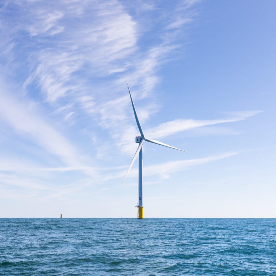 Offshore wind turbine standing in the ocean under a clear blue sky.