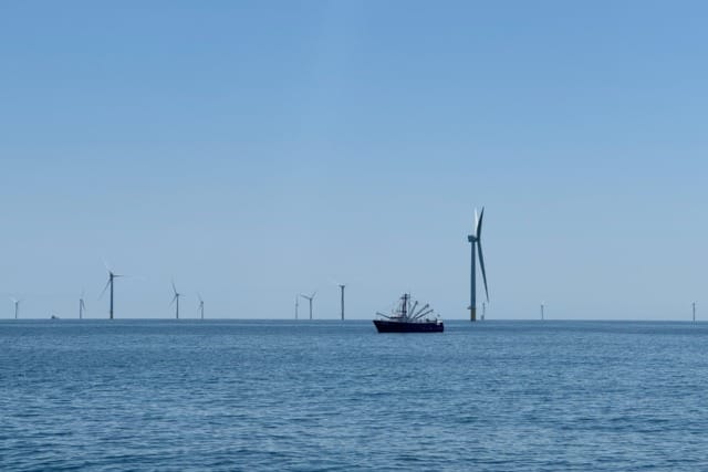 Fishing boat near offshore wind turbines on a calm sea under a clear blue sky.