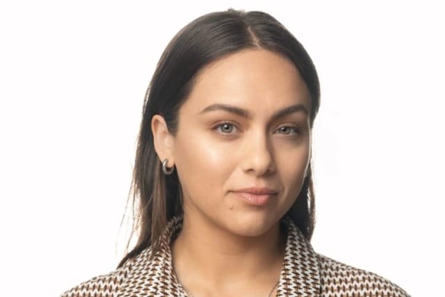 Person with long hair wearing a patterned shirt against a plain white background.