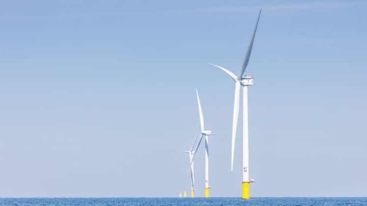 Offshore wind turbines on a clear day with blue sky and calm sea in the background.