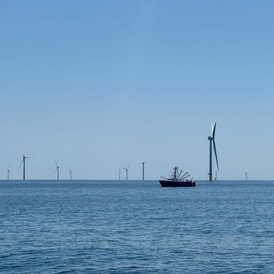 Fishing boat sailing near offshore wind turbines on a clear day.