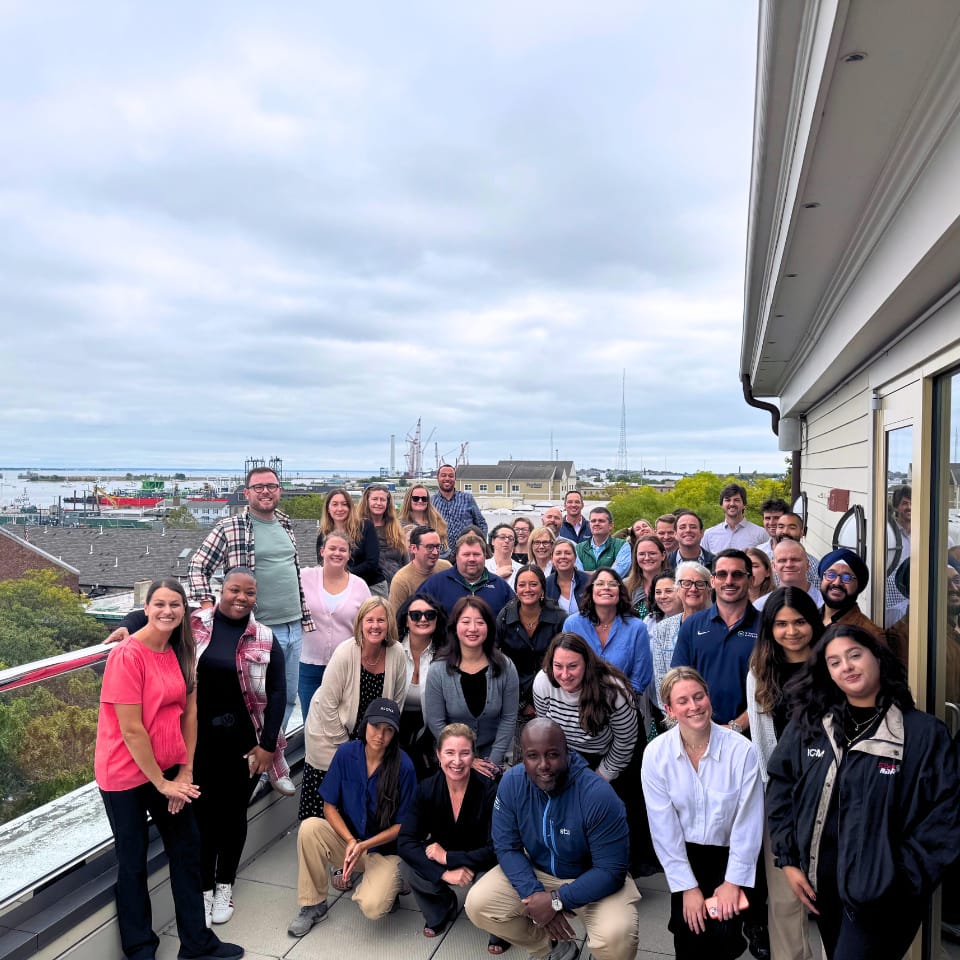 Group of people posing on a rooftop with a coastal background and cloudy sky