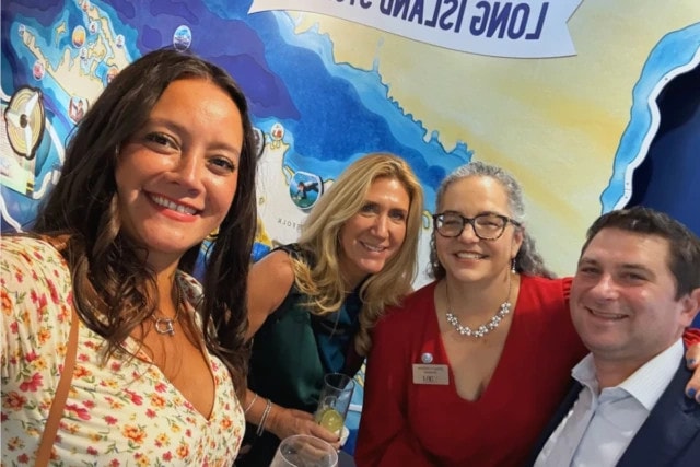 Four people smiling together at a social gathering in front of a colorful map display.